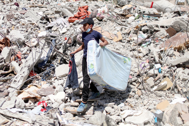 A Palestinian boy carries a mattress as he walks amid the debris of a house destroyed in Israeli air strikes during Israeli-Palestinian fighting, in Gaza City June 2, 2021. REUTERS/Mohammed Salem