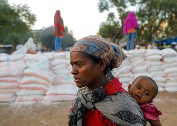 A woman carries an infant as she queues in line for food, at the Tsehaye primary school, which was turned into a temporary shelter for people displaced by conflict, in the town of Shire, Tigray region, Ethiopia, March 15, 2021. Picture taken March 15, 2021. REUTERS/Baz Ratner