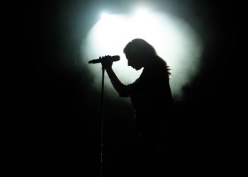 Black silhouette of female singer with white spotlights in the background.