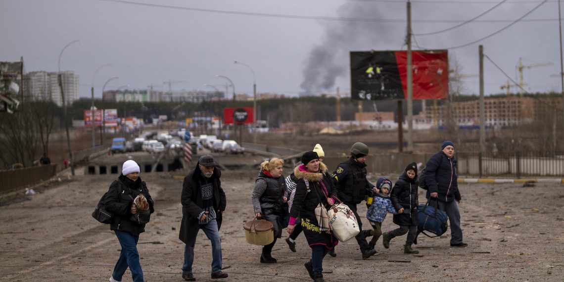 A Ukrainian police officer helps people as artillery echoes nearby while fleeing Irpin in the outskirts of Kyiv, Ukraine, Monday, March 7, 2022. Russia announced yet another cease-fire and a handful of humanitarian corridors to allow civilians to flee Ukraine. Previous such measures have fallen apart and Moscow’s armed forces continued to pummel some Ukrainian cities with rockets Monday. (AP Photo/Emilio Morenatti)