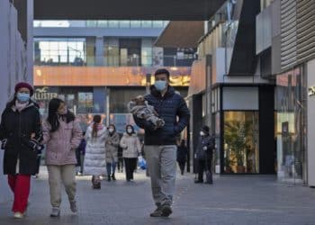 A woman wearing a face mask looks at masked man holding a dog as they walk through a reopened open air shopping mall in Beijing, Sunday, Dec. 4, 2022. China on Sunday reported two additional deaths from COVID-19 as some cities move cautiously to ease anti-pandemic restrictions amid increasingly vocal public frustration over the measures. (AP Photo/Andy Wong)