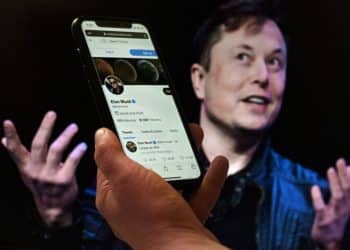 (FILES) In this file photo taken on April 14, 2022 a phone screen displays the Twitter account of Elon Musk with a photo of him shown in the background, in Washington, DC. - The Twitter accounts of several journalists suspended after Musk accused them of endangering his family were reinstated on December 17, 2022, but some said the billionaire owner offered full use of the platform only if they deleted posts about tracking his location. Musk had drawn anger and warnings from the EU and UN after suspending the accounts of more than a half-dozen prominent journalists from The New York Times, CNN, The Washington Post and other outlets. (Photo by Olivier DOULIERY / AFP)